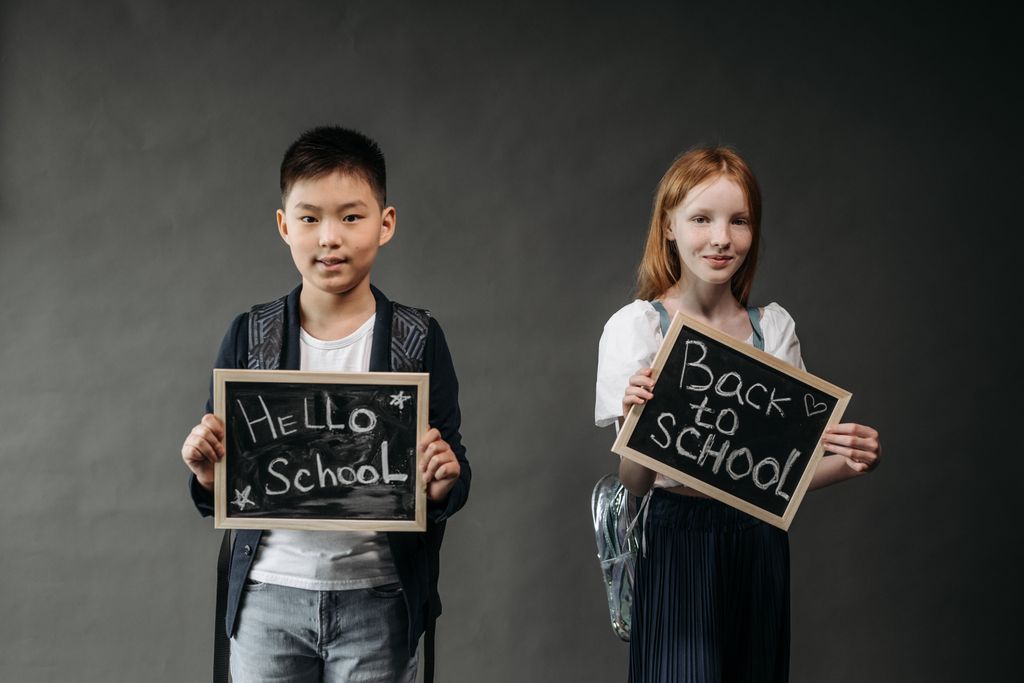 Two kids with black boards saying Hello School and Back to School