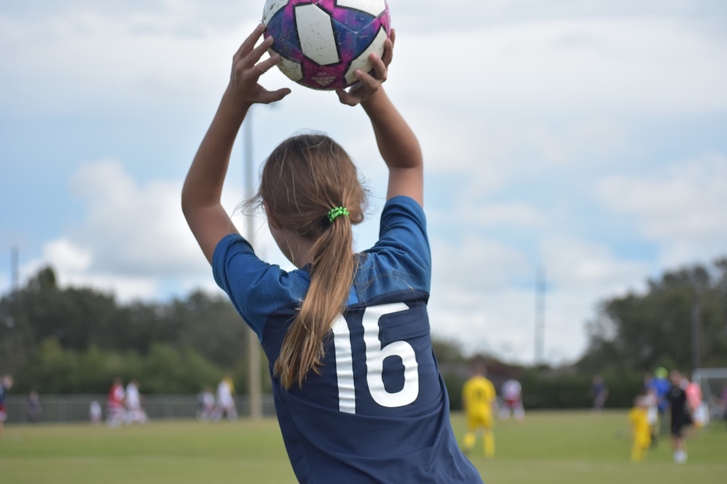 A girl's back with a soccer ball overhead