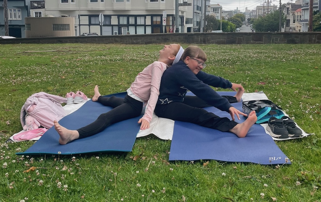 Two girls back to pack in a wide angle partner yoga pose