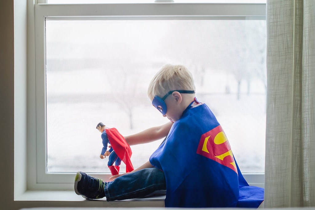 A boy in a Superman cape and mask playing with a superman figure