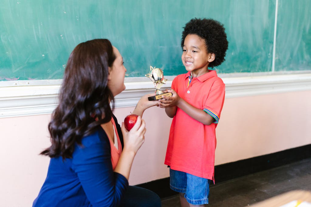 A teacher receiving an apple and a trophy from a child