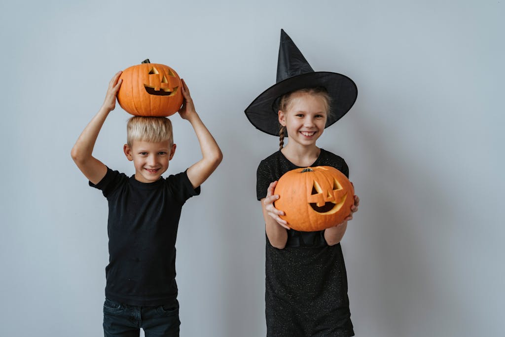 One boy and one girl wearing a witch hat holding carved pumpkins