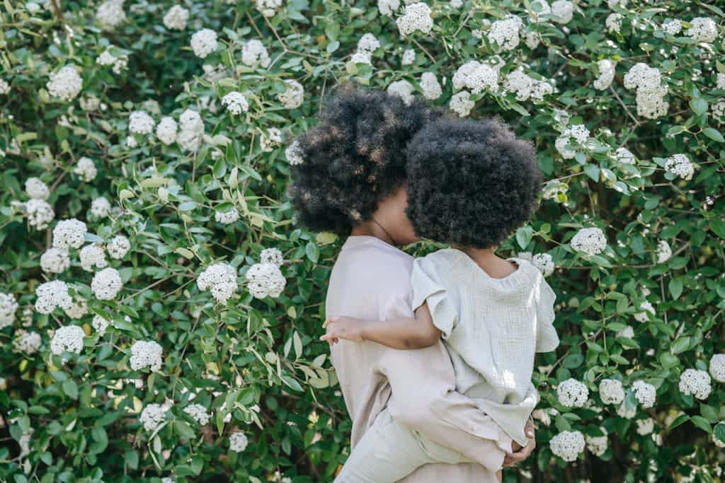 A black mother and daughter in front of white and green flowers
