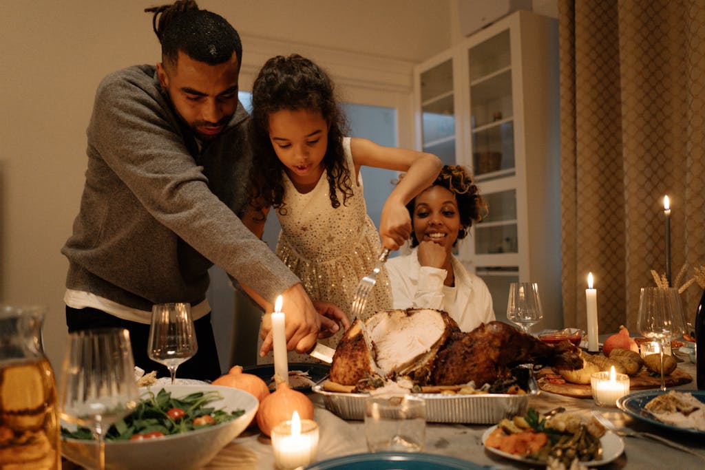 A dad helping his daughter cut a Thanksgiving turkey with mom seated nearby
