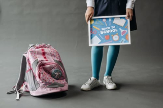 A girl holding a Back to School sign next to a pink backpack.
